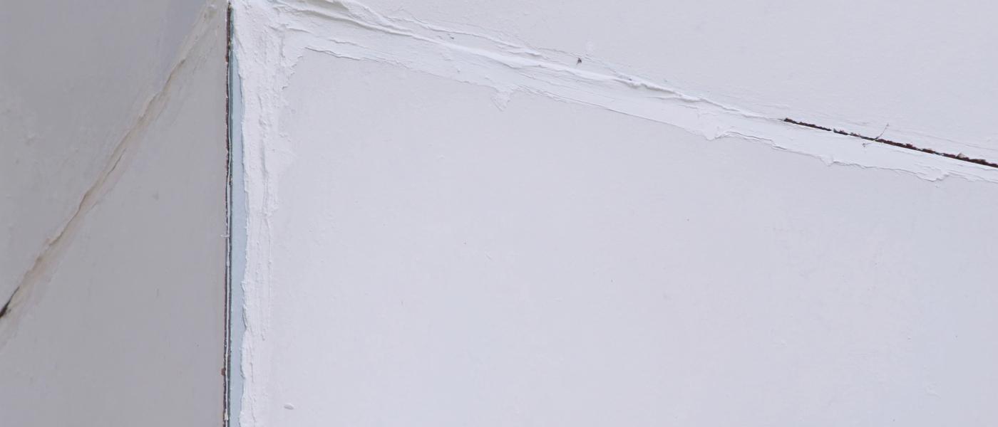 A drywall corner joint coated in fresh white joint compound, feathered out along both wall faces