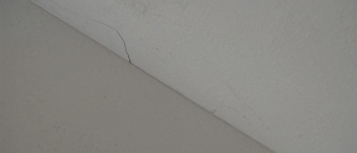 A long hairline crack running along a taped joint at the junction of a ceiling and wall in an older home