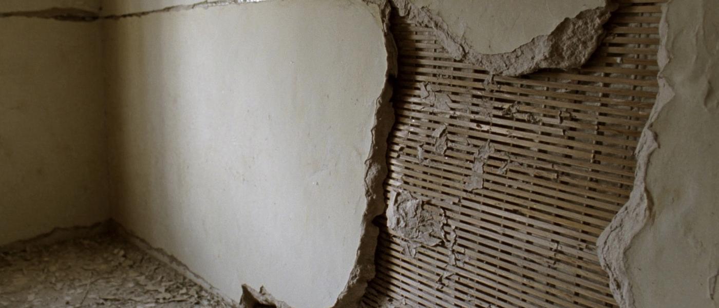 Broken plaster fallen away from an interior wall to expose narrow horizontal wooden lath strips behind