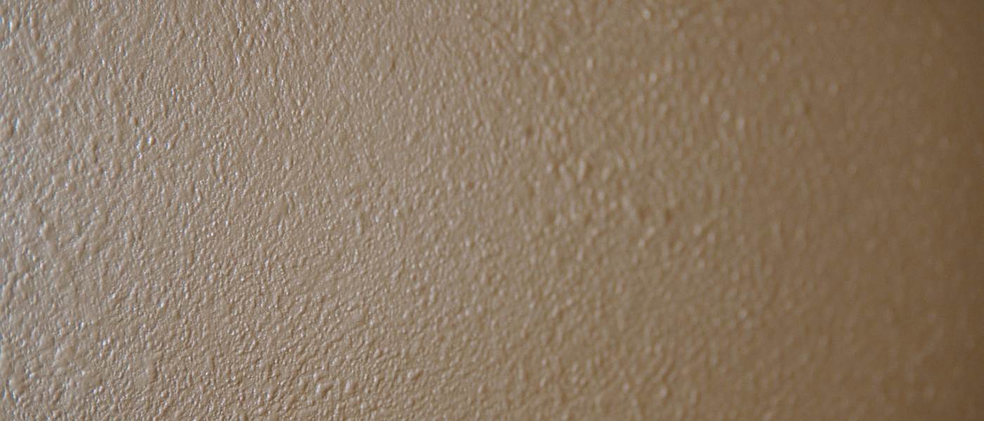Extreme close view of orange peel drywall texture on a painted wall lit by low raking sunlight so each bump casts a shadow